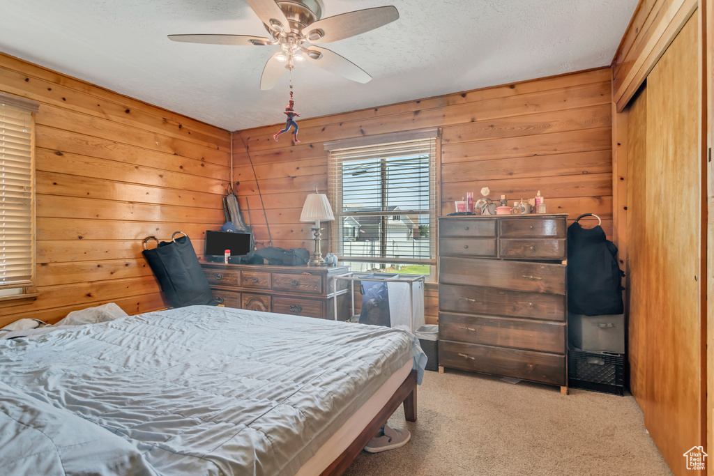 Carpeted bedroom with wood walls, a textured ceiling, and ceiling fan