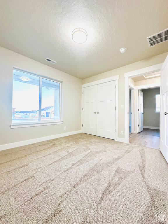 Unfurnished bedroom featuring a closet, light carpet, and a textured ceiling