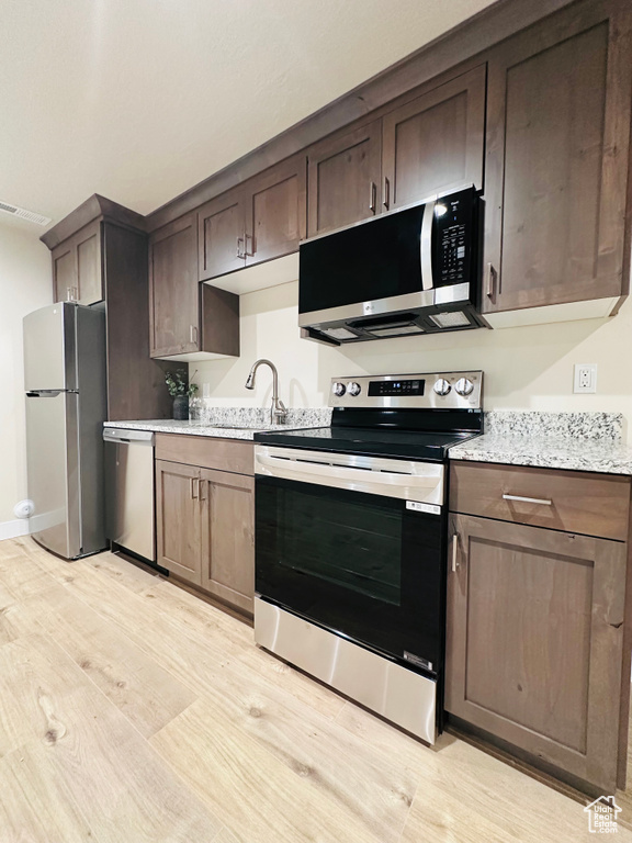 Kitchen with light stone counters, appliances with stainless steel finishes, sink, and dark brown cabinets