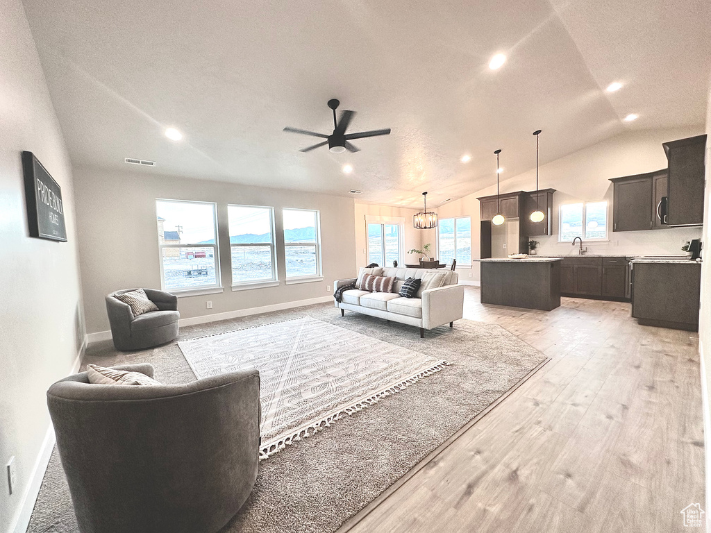 Living room with lofted ceiling, a textured ceiling, light hardwood / wood-style flooring, ceiling fan with notable chandelier, and sink