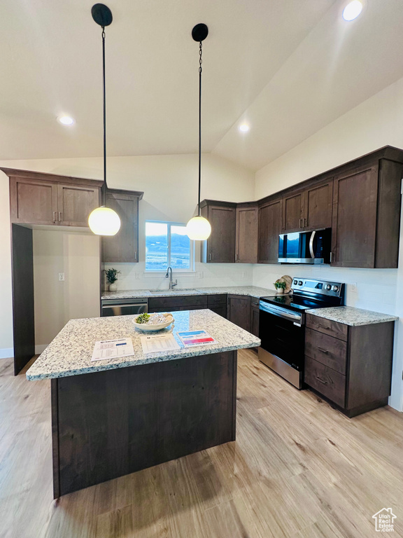 Kitchen with light wood-type flooring, a center island, stainless steel appliances, vaulted ceiling, and light stone counters