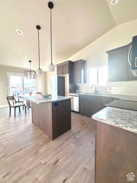 Kitchen with lofted ceiling, decorative backsplash, a kitchen island, pendant lighting, and light stone counters