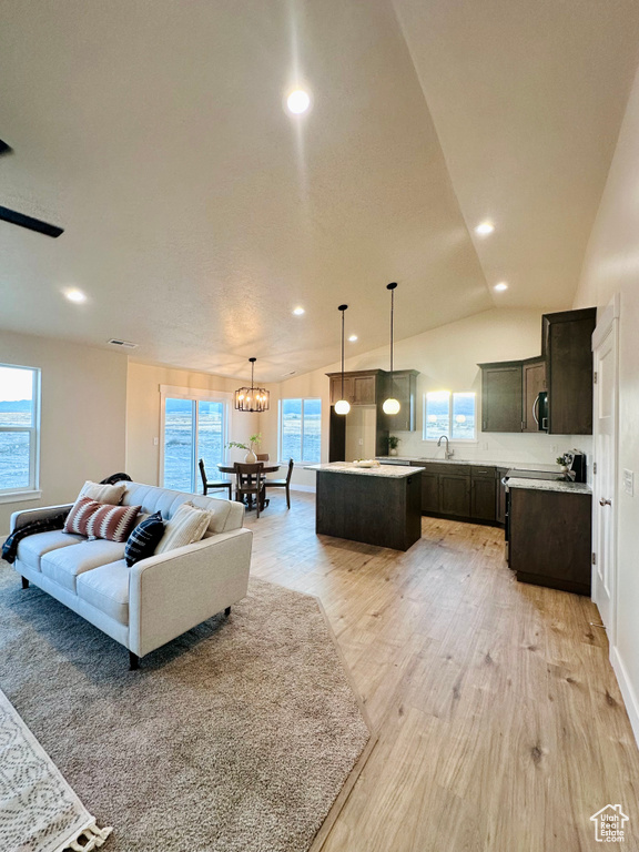 Living room featuring lofted ceiling, a chandelier, light hardwood / wood-style floors, and a healthy amount of sunlight