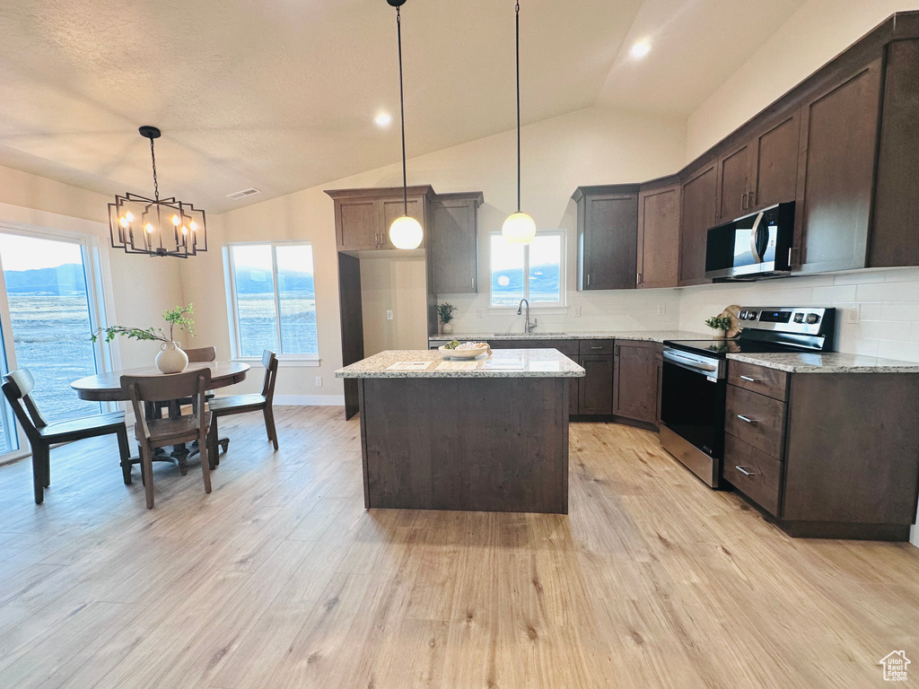 Kitchen with a kitchen island, stainless steel appliances, light stone countertops, vaulted ceiling, and pendant lighting