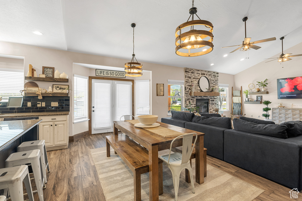 Dining room featuring lofted ceiling, light hardwood / wood-style floors, ceiling fan with notable chandelier, and a fireplace