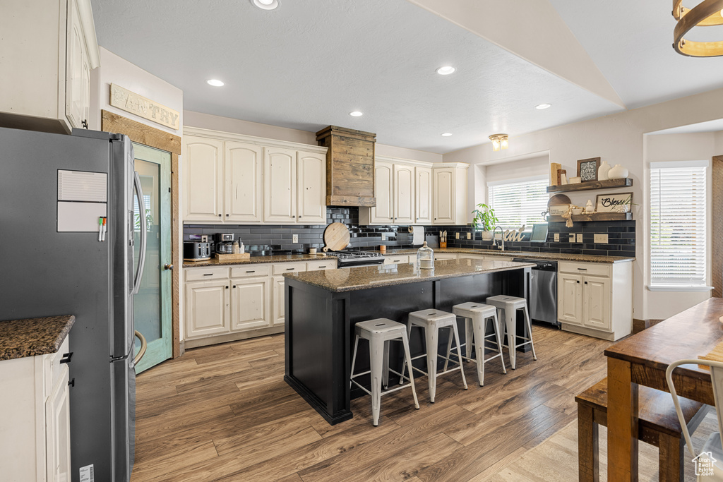 Kitchen with a kitchen island, appliances with stainless steel finishes, decorative backsplash, and light hardwood / wood-style floors