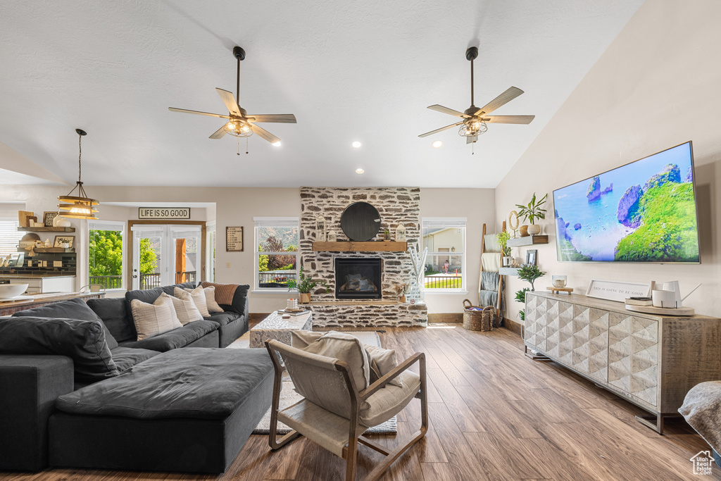 Living room featuring french doors, ceiling fan, a stone fireplace, wood-type flooring, and high vaulted ceiling