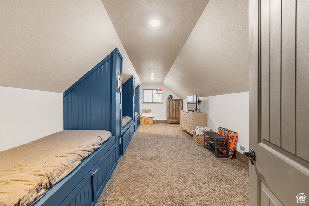 Bedroom featuring light carpet, vaulted ceiling, and a textured ceiling