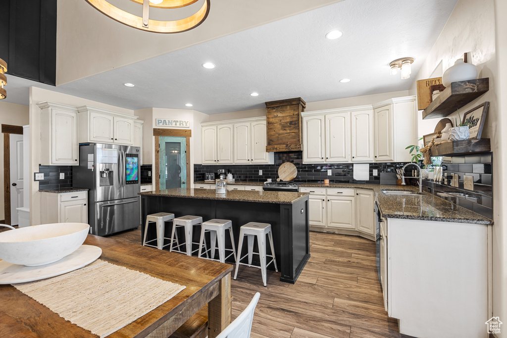 Kitchen featuring tasteful backsplash, white cabinets, a center island, stainless steel refrigerator with ice dispenser, and sink