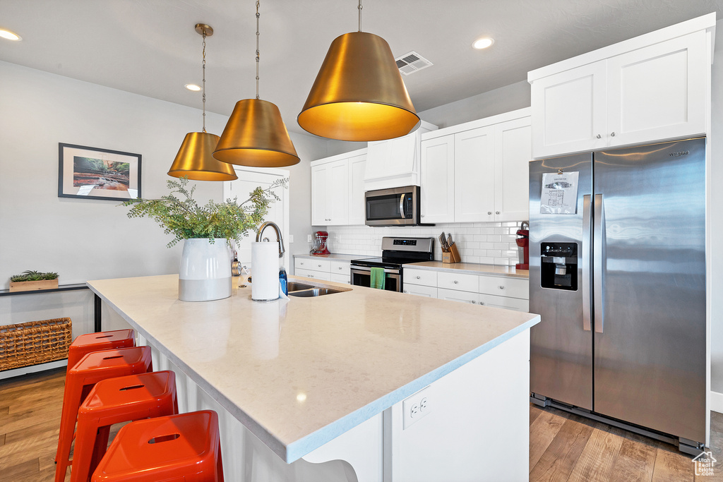 Kitchen featuring light hardwood / wood-style flooring, backsplash, an island with sink, appliances with stainless steel finishes, and sink