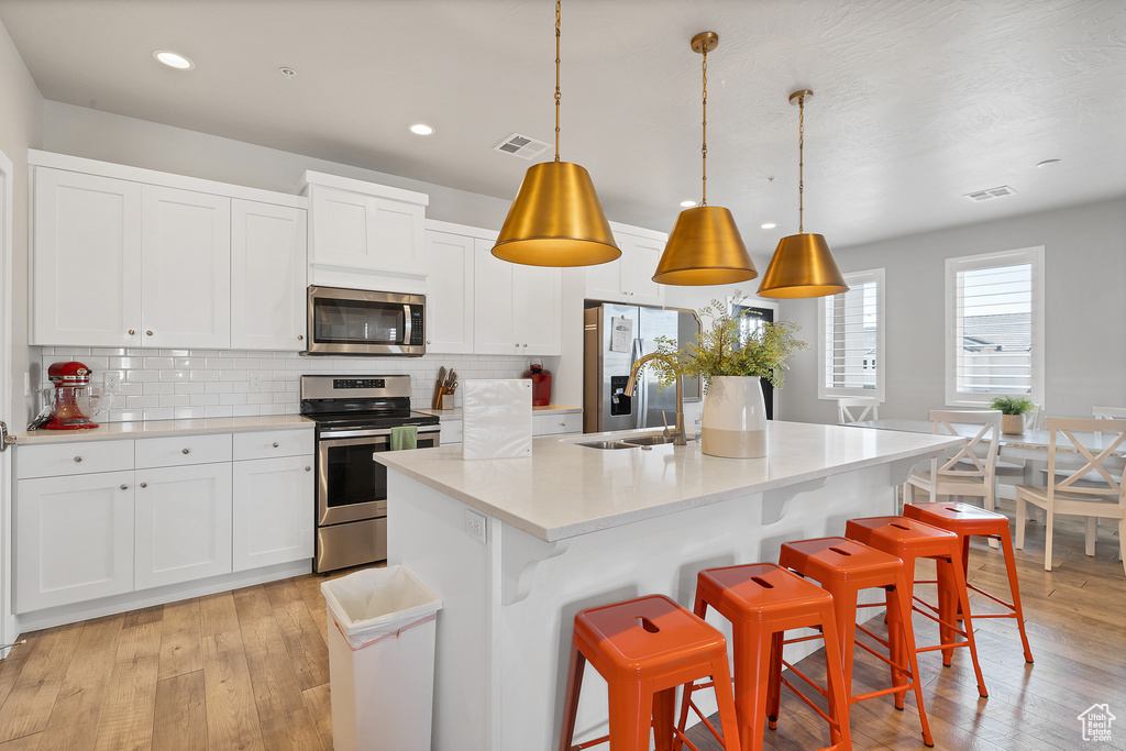 Kitchen with backsplash, decorative light fixtures, light hardwood / wood-style flooring, and appliances with stainless steel finishes