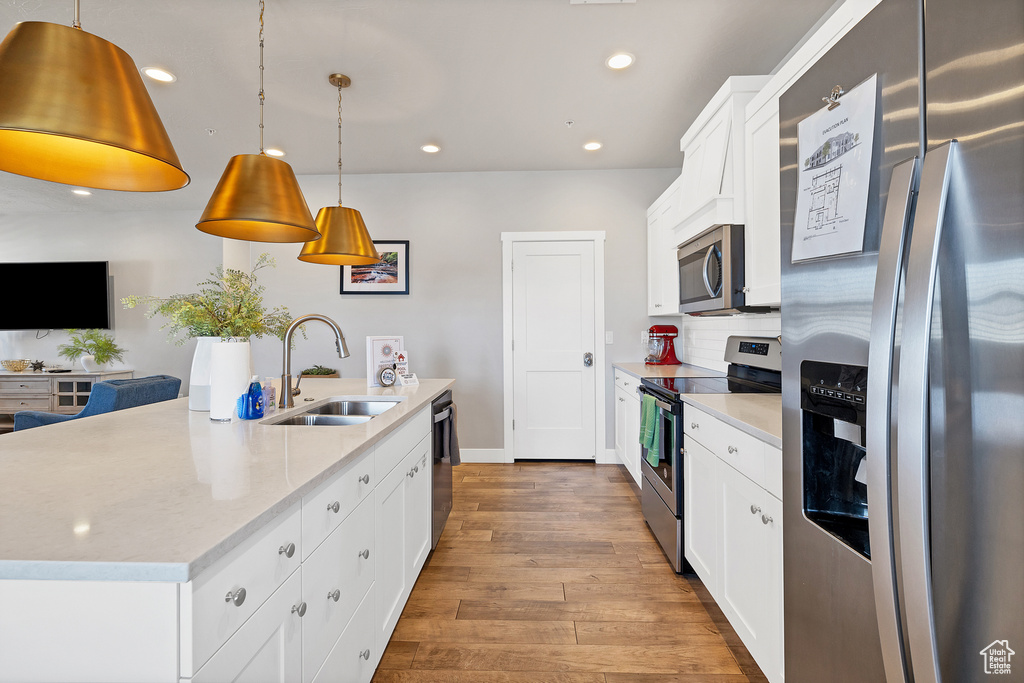 Kitchen with white cabinetry, stainless steel appliances, light hardwood / wood-style floors, hanging light fixtures, and sink