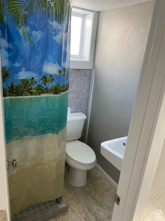 Bathroom with tile walls, tile flooring, and toilet