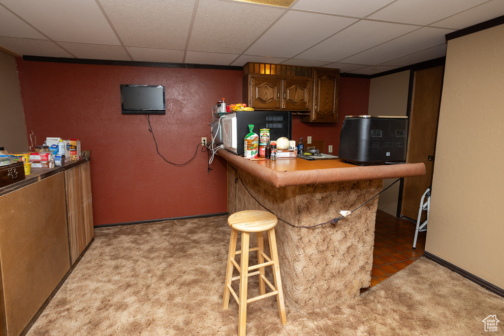 Kitchen with light carpet, a drop ceiling, a kitchen bar, and kitchen peninsula