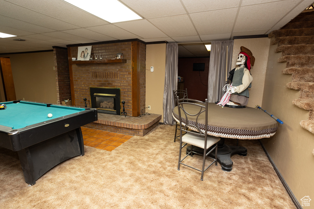 Recreation room featuring carpet flooring, pool table, a brick fireplace, brick wall, and a paneled ceiling