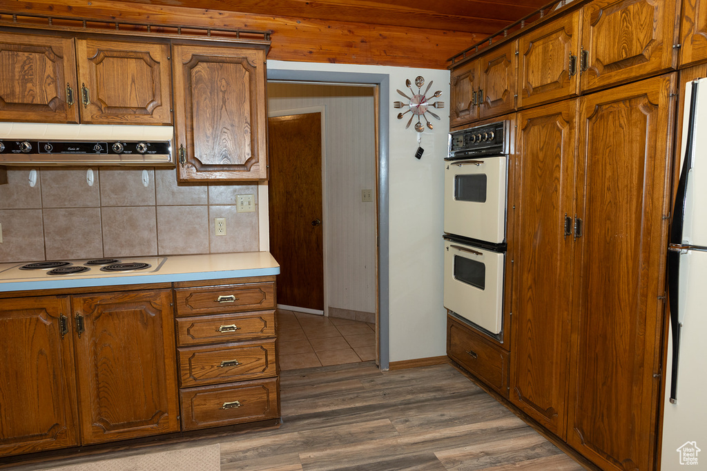 Kitchen with ventilation hood, wood-type flooring, backsplash, and white appliances