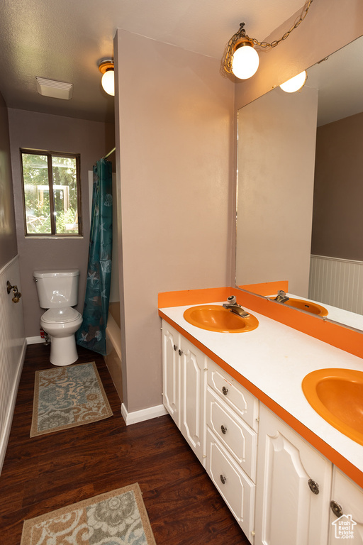 Full bathroom with hardwood / wood-style flooring, double vanity, shower / tub combo, toilet, and a textured ceiling