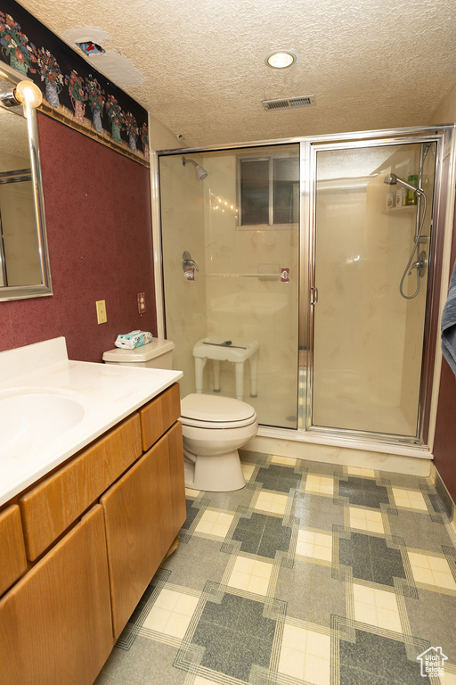 Bathroom featuring tile patterned flooring, an enclosed shower, a textured ceiling, toilet, and vanity