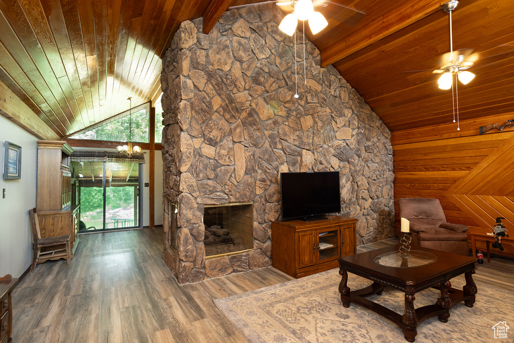 Unfurnished living room with wood walls, wooden ceiling, a stone fireplace, and hardwood / wood-style floors