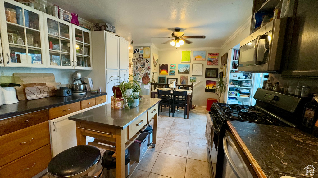 Kitchen with gas stove, light tile patterned flooring, white cabinetry, ceiling fan, and ornamental molding