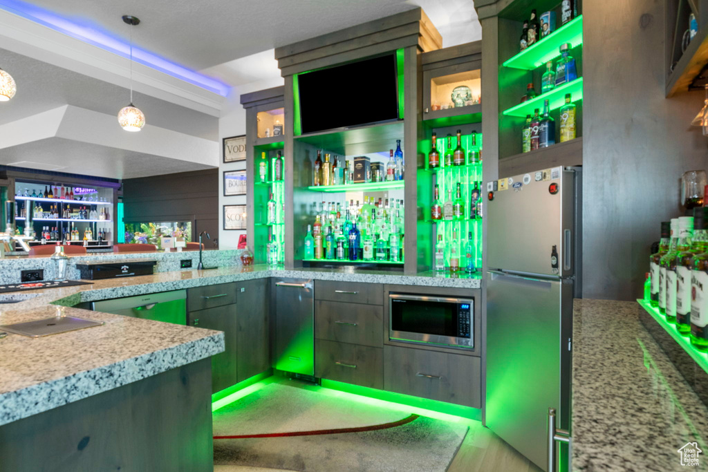 Bar featuring decorative light fixtures, green cabinetry, light stone counters, and stainless steel appliances