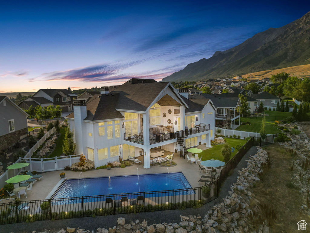 Back house at dusk featuring a mountain view, a patio, pool water feature, and a community pool