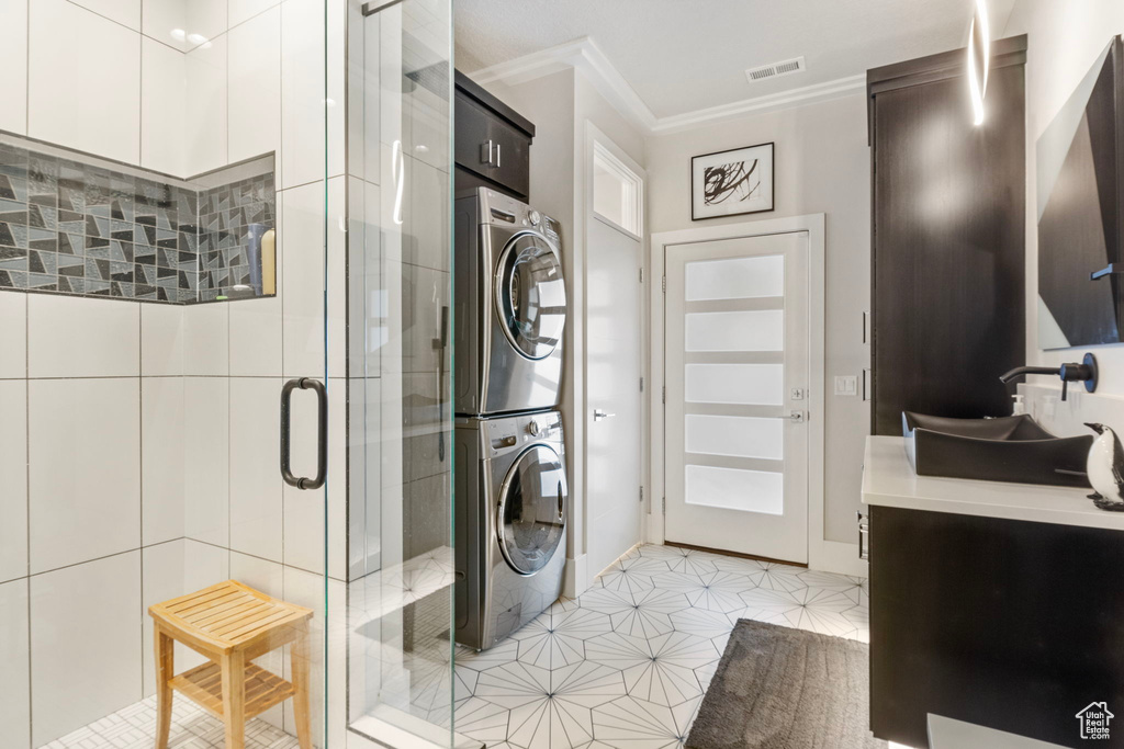 Washroom featuring stacked washer and clothes dryer, ornamental molding, and light tile patterned floors