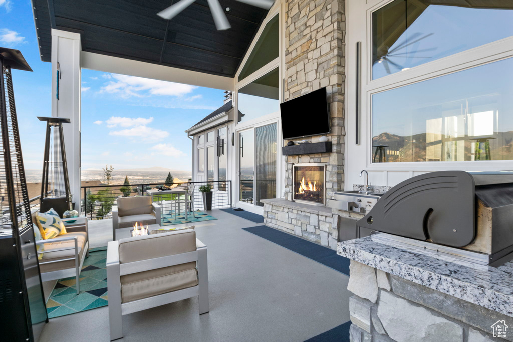 View of patio featuring an outdoor stone fireplace, ceiling fan, and exterior kitchen