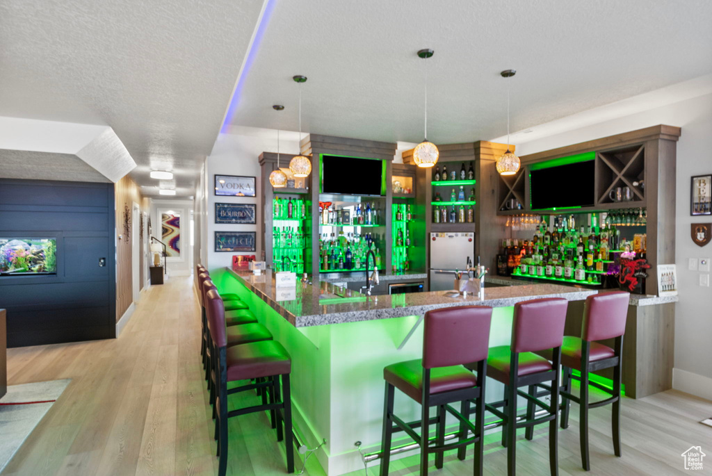 Interior space with a kitchen bar, light wood-type flooring, decorative light fixtures, and a textured ceiling