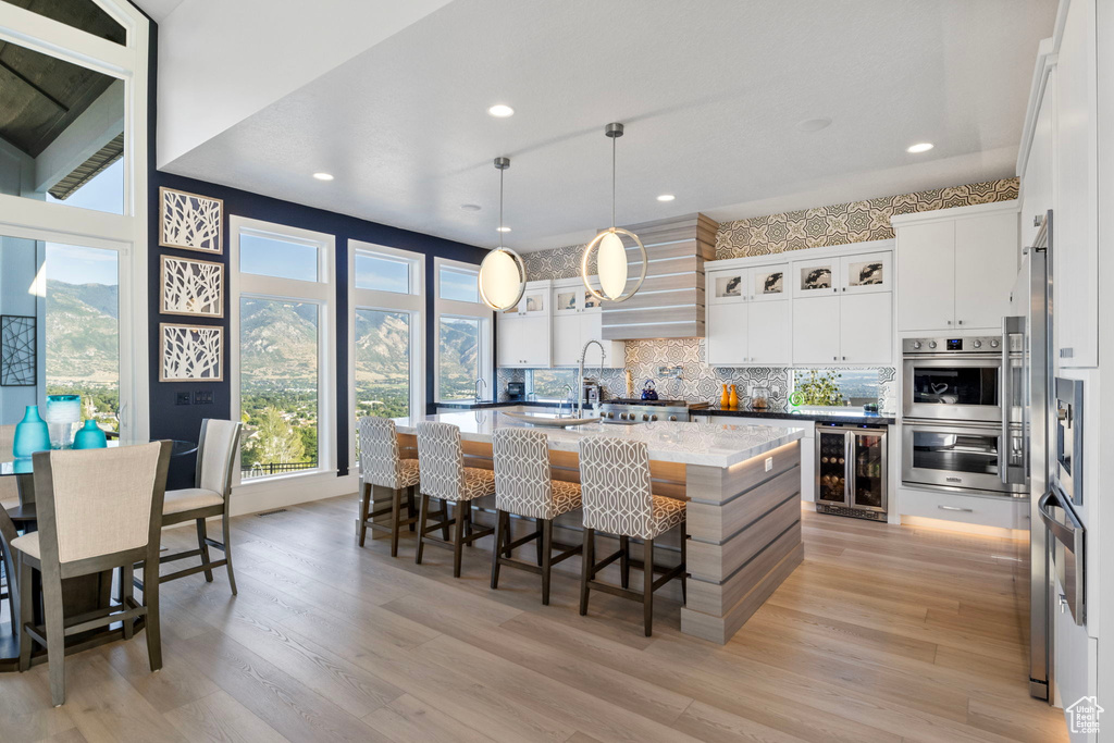 Kitchen featuring light hardwood / wood-style flooring, tasteful backsplash, hanging light fixtures, a kitchen island with sink, and stainless steel double oven