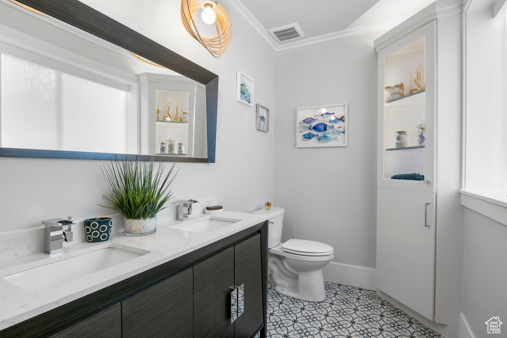 Bathroom featuring tile patterned floors, crown molding, toilet, and double sink vanity