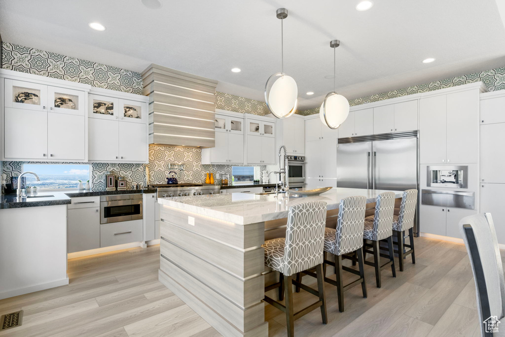 Kitchen featuring light wood-type flooring, an island with sink, hanging light fixtures, appliances with stainless steel finishes, and decorative backsplash