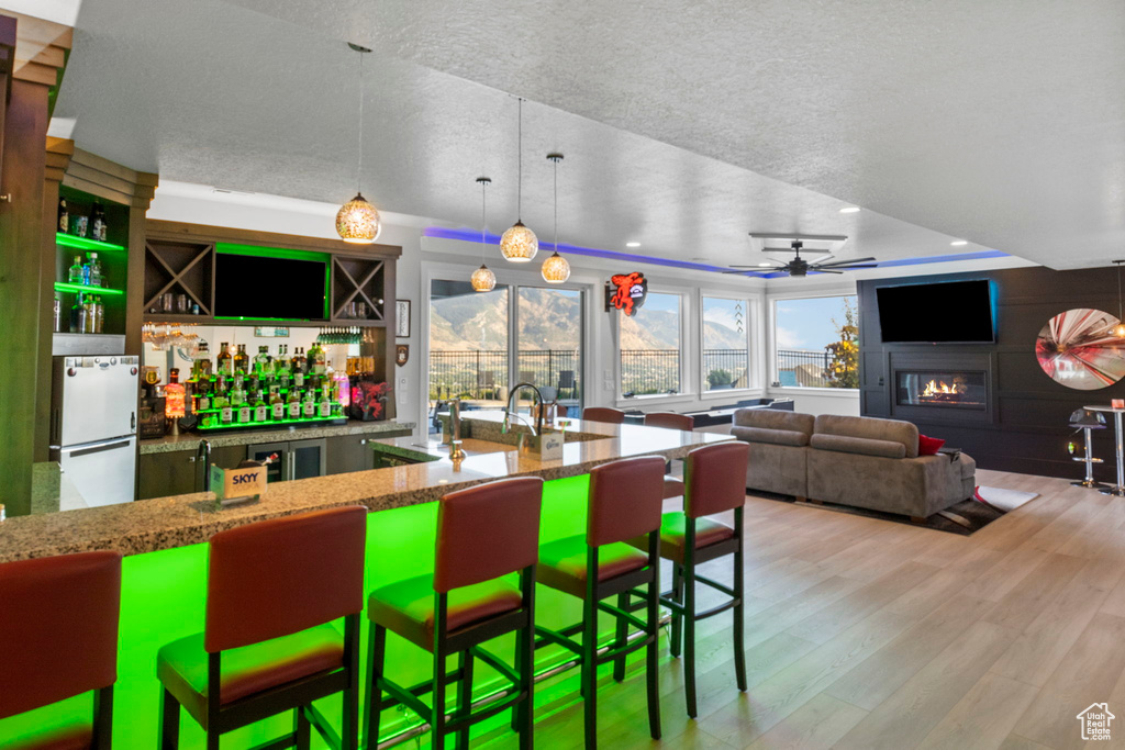 Kitchen with hanging light fixtures, stone counters, light wood-type flooring, fridge, and a raised ceiling