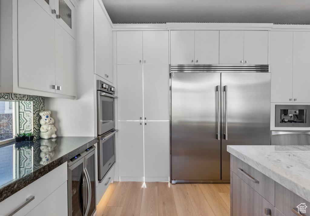 Kitchen with built in appliances, white cabinetry, dark stone countertops, and light hardwood / wood-style floors