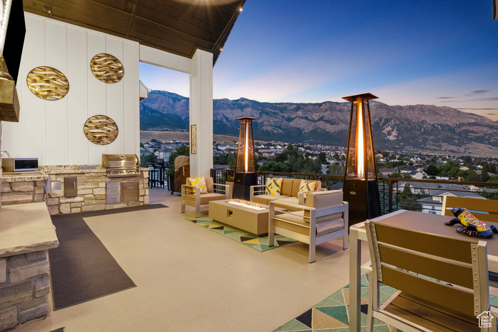 Patio terrace at dusk featuring grilling area, an outdoor kitchen, a mountain view, and an outdoor hangout area