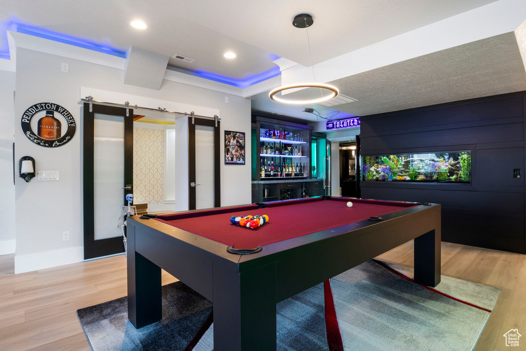 Rec room featuring a barn door, light wood-type flooring, a tray ceiling, ornamental molding, and billiards