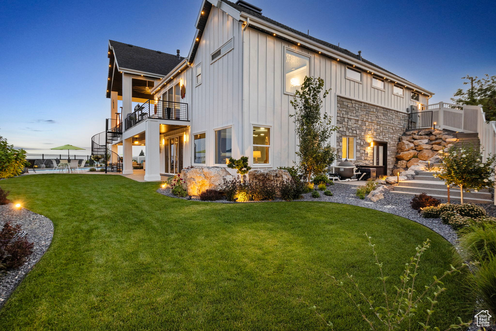 Back house at dusk with a balcony, a patio, and a lawn