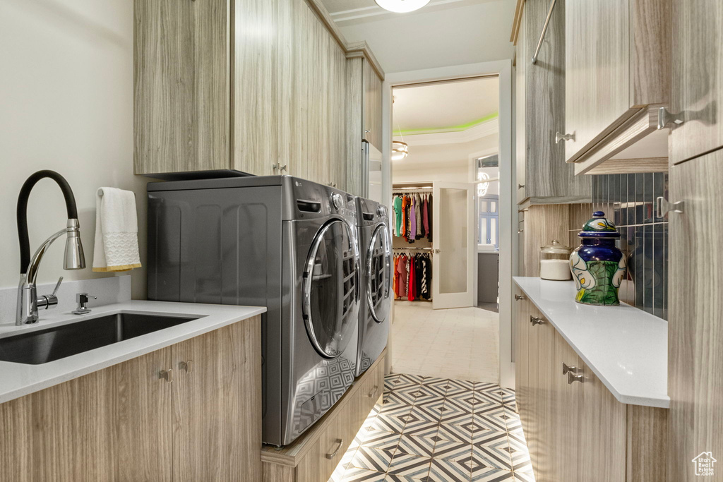 Clothes washing area with washer and clothes dryer, crown molding, sink, cabinets, and light tile patterned floors