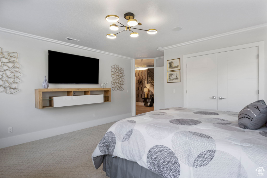 Carpeted bedroom with an inviting chandelier, crown molding, and a closet