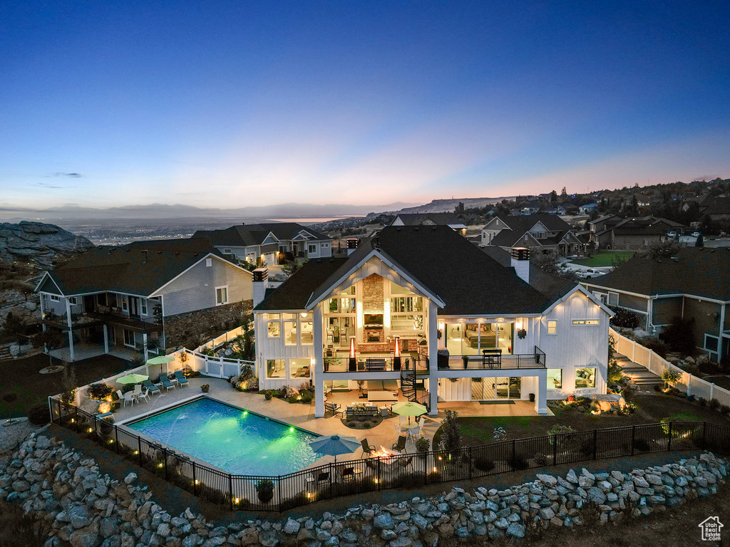 Back house at dusk featuring a patio, a balcony, and a fenced in pool