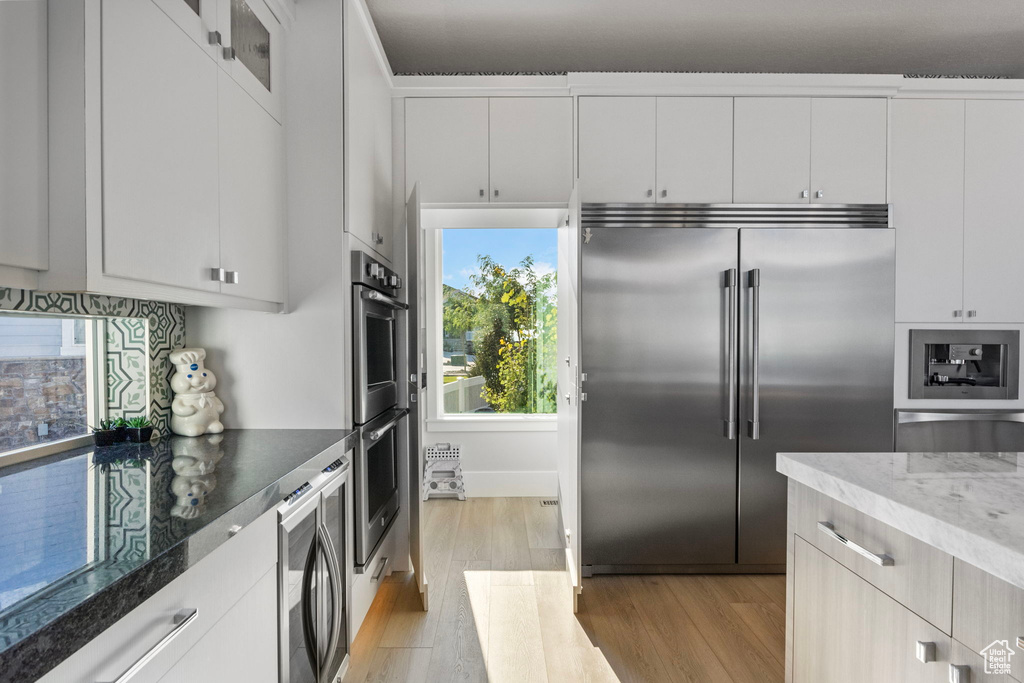 Kitchen with appliances with stainless steel finishes, light hardwood / wood-style flooring, and white cabinetry