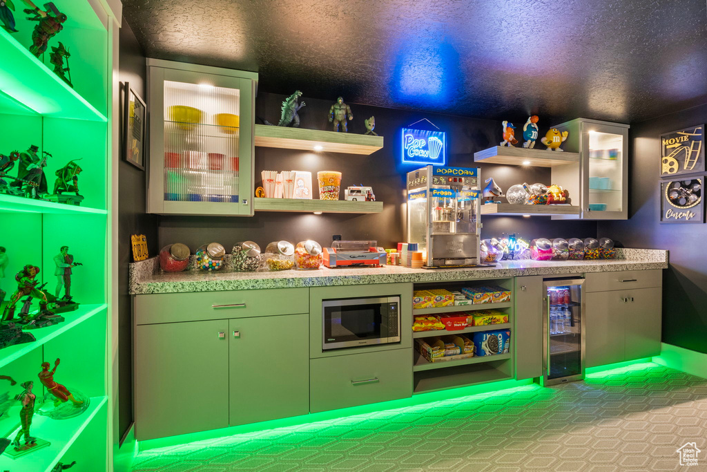 Bar with tile patterned floors, stainless steel microwave, a textured ceiling, and beverage cooler