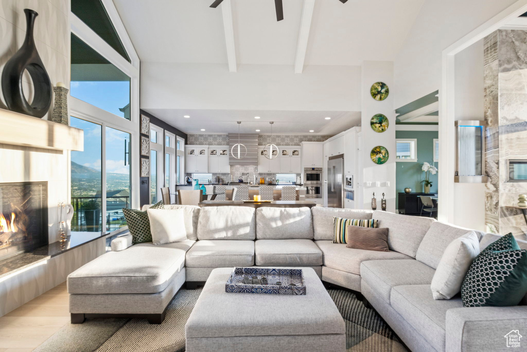 Living room featuring a premium fireplace, ceiling fan, high vaulted ceiling, and light hardwood / wood-style floors