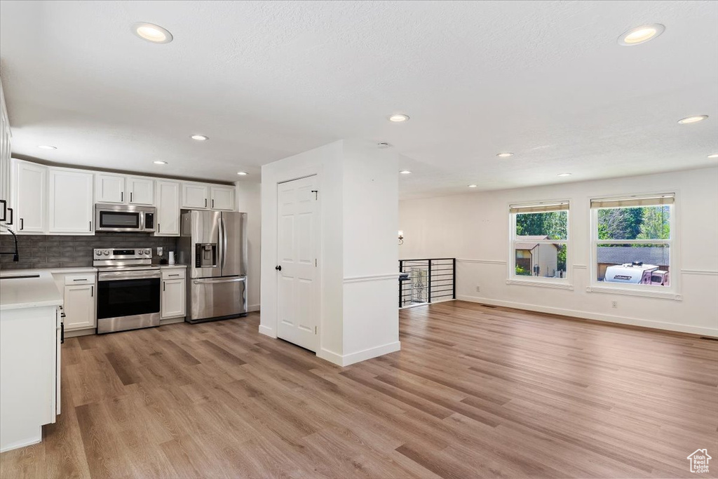 Kitchen with white cabinetry, stainless steel appliances, tasteful backsplash, and light wood-type flooring