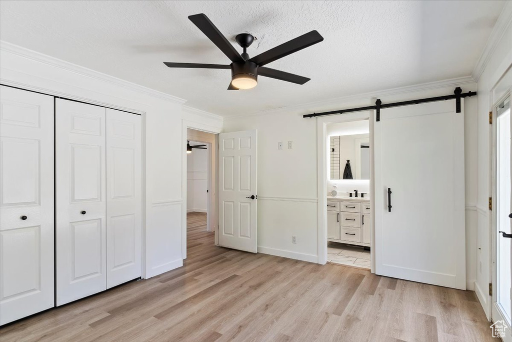 Unfurnished bedroom with a closet, connected bathroom, light hardwood / wood-style floors, a barn door, and ceiling fan