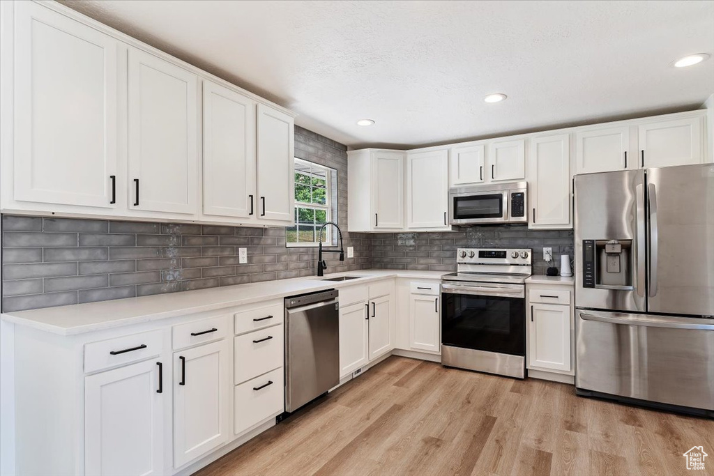 Kitchen featuring backsplash, white cabinetry, stainless steel appliances, and light hardwood / wood-style floors