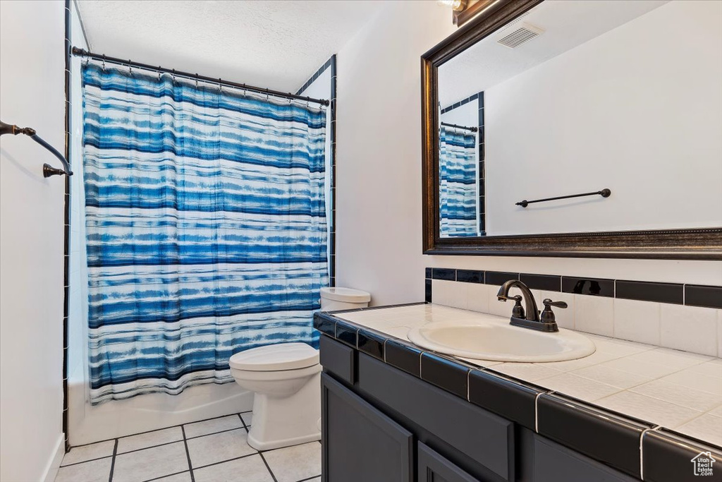 Full bathroom with backsplash, shower / tub combo with curtain, toilet, tile patterned floors, and vanity