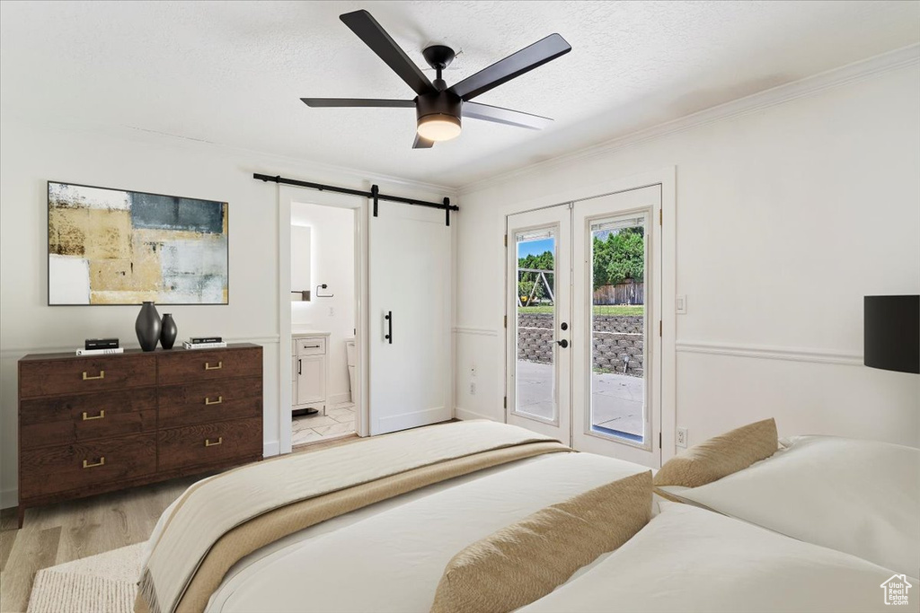 Bedroom featuring connected bathroom, a barn door, access to outside, light wood-type flooring, and ceiling fan