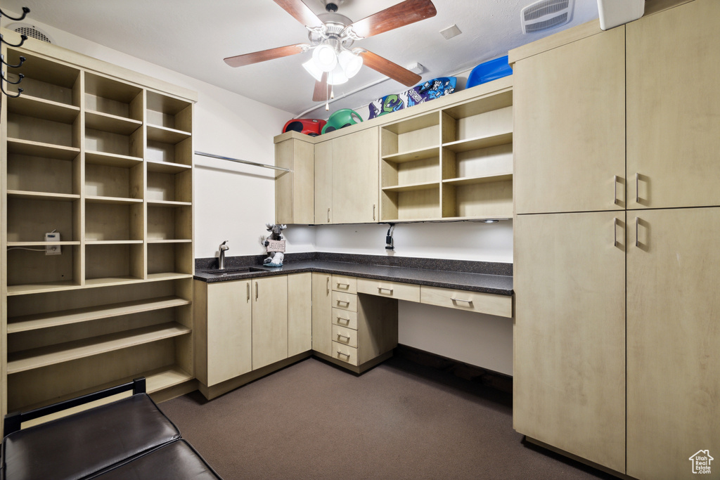 Unfurnished office with built in desk, sink, ceiling fan, and dark colored carpet