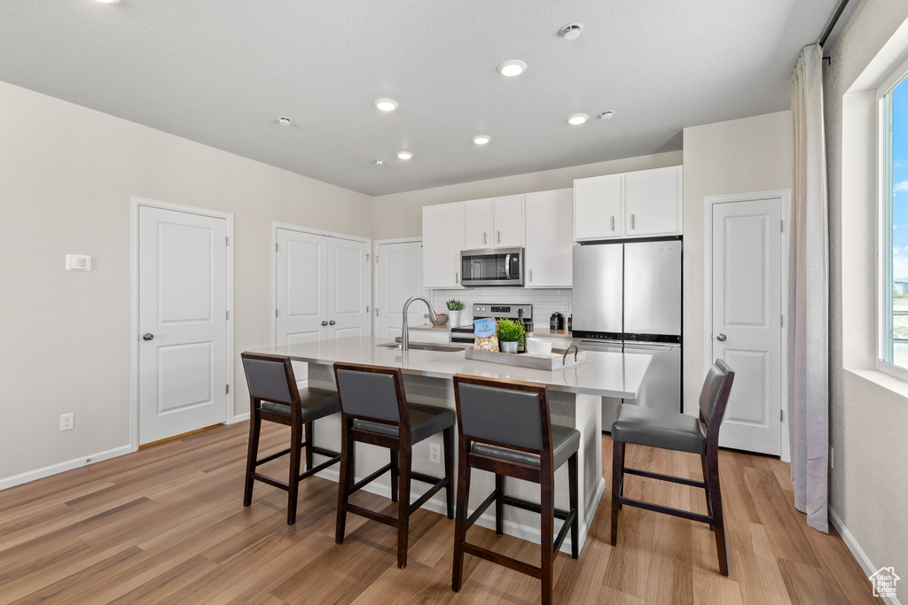 Kitchen featuring a kitchen bar, appliances with stainless steel finishes, sink, light wood-type flooring, and an island with sink